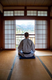 Young man wearing kimono sitting in traditional Japanese living room with tatami mats and shoji