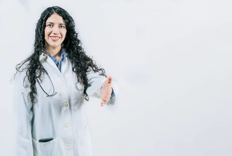 Latin female doctor shaking hands at the camera gesturing welcome. Smiling female doctor gesturing