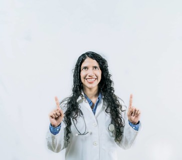 Cheerful female doctor pointing up isolated. Young female doctor looking and pointing at promotion