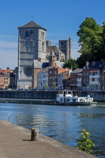 16th century Gothic Notre-Dame collegiate church and riverboat on the Meuse river in the city Huy,