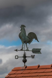 Metallic weather vane on a tiled roof, dramatic sky in the background, Baden-Württemberg, Germany