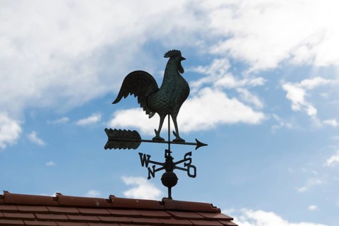 Metal weather vane on a roof surrounded by blue sky and clouds, Baden-Württemberg, Germany