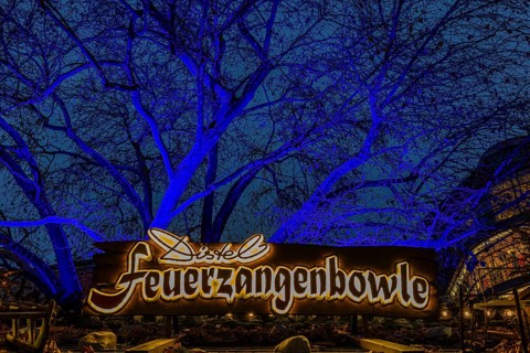 Sales stand for Feuerzangenbowle, above a deciduous tree illuminated with blue light,