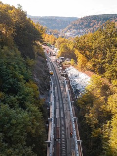 Construction work on railroad tracks in the middle of an autumn forest with excavators and hills,