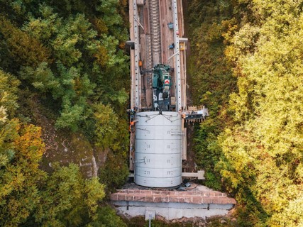 Bird's eye view shows crane over tunnel on a railway line surrounded by trees, construction of