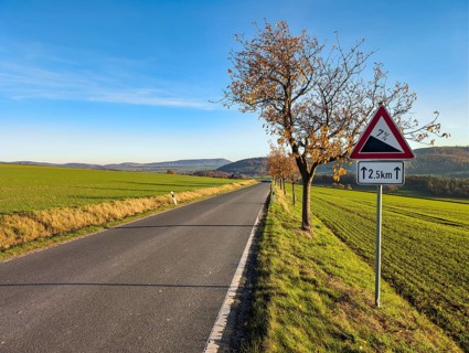 Country road through hilly, agricultural landscape, road sign warns of slopes, slopes, sunny autumn