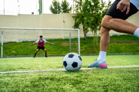 Football player preparing to shoot a penalty kick with the ball on the artificial turf, facing a