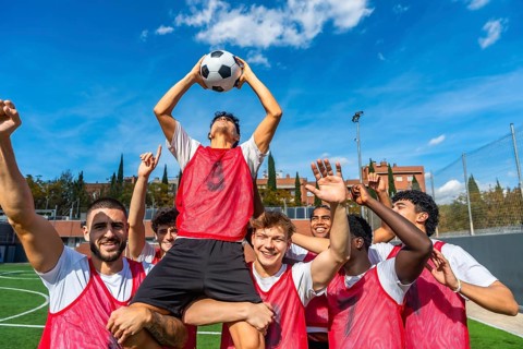 Young male soccer team members celebrating a goal or game victory on a green athletic field,