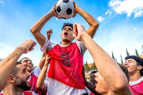 Young diverse men's soccer team members are cheering loud with fists raised and one player is