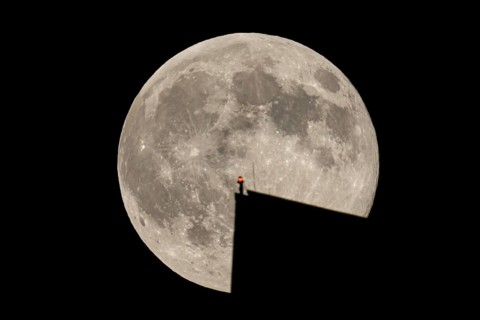 The full moon sweeps along the Frankfurt evening sky and passes the tip of the European Central