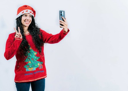Happy young latin woman in Christmas sweater taking selfies isolated. Funny girl in Christmas hat