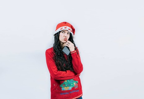 Young woman in christmas sweater thoughtful holding cell phone isolated. Girl in christmas hat
