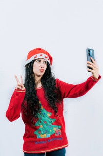 Funny latin girl in Christmas hat taking selfies and making gestures isolated. Cheerful young woman