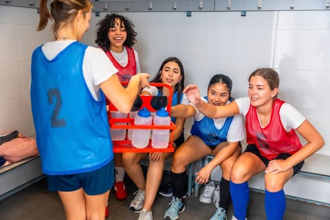 Teenagers from a diverse girls soccer team taking a water break and hydrating, showing friendship,