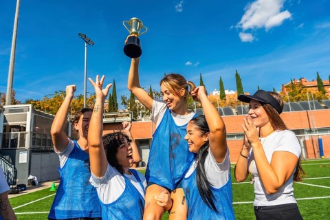 Happy young women soccer players celebrating victory on a sunny outdoor field, lifting the