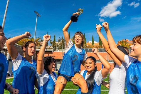 Female athletes sharing joy and success, lifting their teammate holding a trophy after winning a