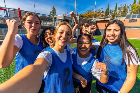 Group of smiling young women players celebrating success and victory on a soccer field, posing for