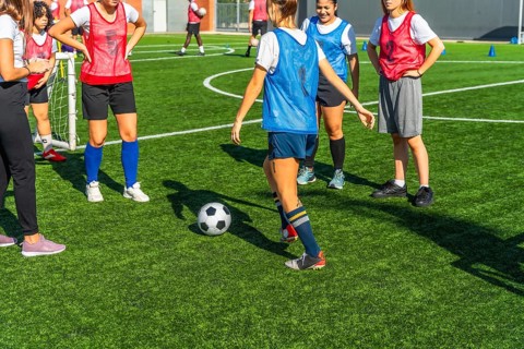 Diverse women soccer players training together on a sunny outdoor turf field, practicing dribbling,