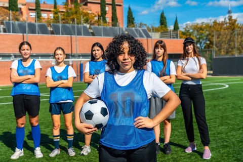 Diverse group of young women, wearing blue vests and sportswear, standing proudly on a green