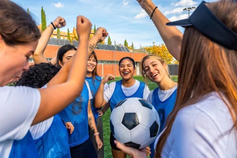 Happy female soccer team players huddling together on the field, raising their fists in