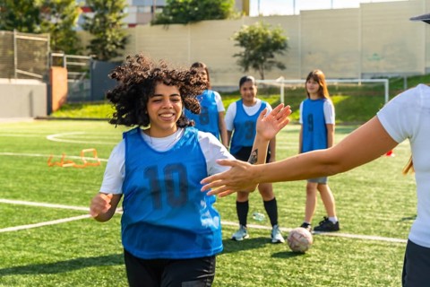 Young female soccer player high fiving her coach on a green artificial turf field, training with