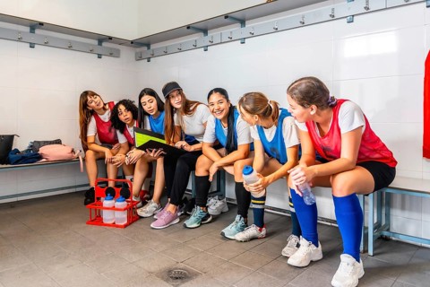 Female athletes wearing sports attire sitting on a bench in a locker room, discussing strategy and