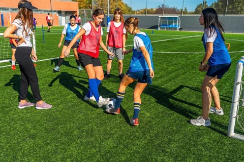 Young women soccer players are practicing passing and dribbling drills on a green artificial turf