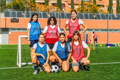 Diverse group of women on a soccer field, some standing and some crouching, wearing jerseys and
