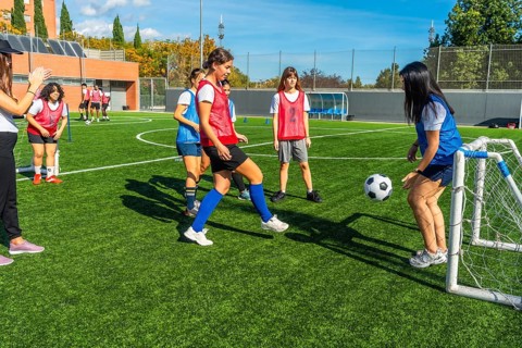 Young females training soccer on an artificial turf field, engaging in a small sided game with a