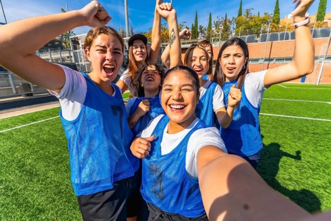 Group of excited multiracial women soccer players in blue vests and white t shirts celebrating