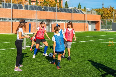 Girls soccer team receiving instructions from their female coach while practicing ball control and