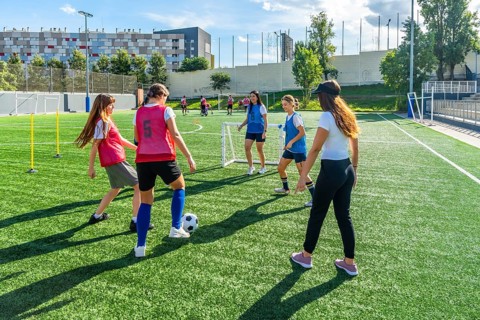 Female soccer teammates training on a sunny artificial turf field, practicing dribbling, passing