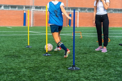 Young woman in a blue bib practicing soccer dribbling skills, maneuvering a ball through training