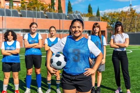 Diverse women's soccer team, featuring a smiling player holding a football, standing proudly on a