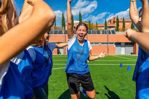 Young women's soccer team celebrating a goal, arms raised and cheering with bright smiles on a