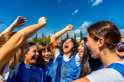 Young women soccer players cheering with arms raised in celebration, smiling and embracing after