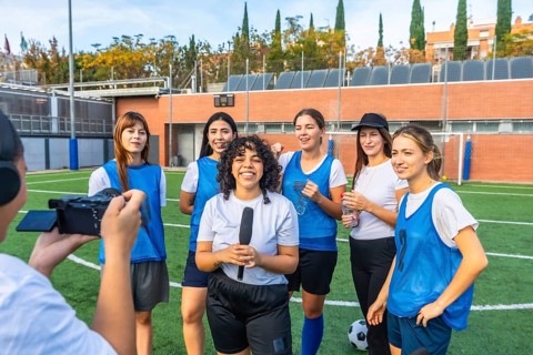 Female football players and their coach standing on a green field after a game, giving an interview