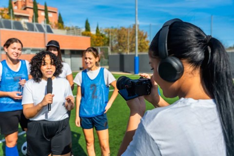Videographer with headphones filming a reporter holding a microphone and interviewing a group of