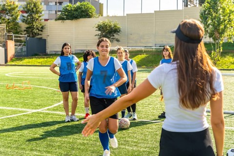 Young women's soccer team participating in a training session on a sunny artificial turf field,