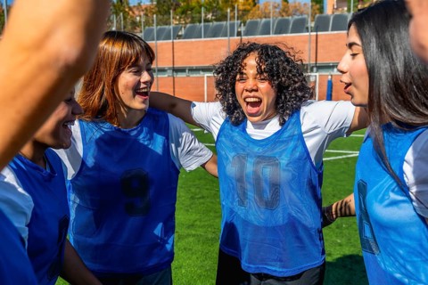 Young diverse women football players joining arms in a huddle, enthusiastically celebrating a