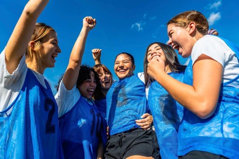 Diverse group of young women soccer players celebrating a goal or victory, raising fists and