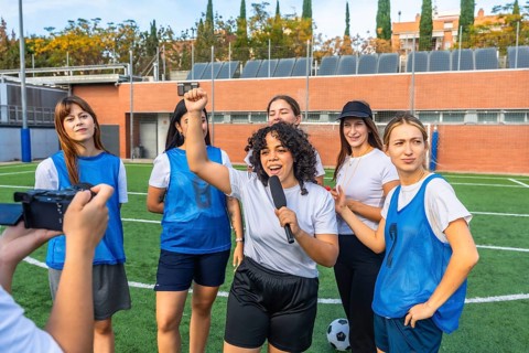 Happy young women's soccer team and coach giving an interview on artificial turf field, celebrating