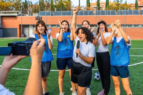 Women's football team standing on grass field, cheering and celebrating a win as one player holds a