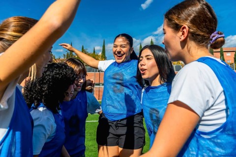 Group of diverse women's soccer players huddling on the field, actively celebrating their success