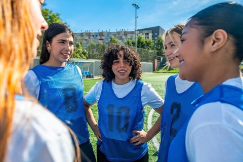 Diverse young women soccer team huddling on a green sports field, collaborating and discussing