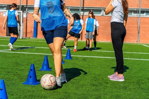 Young women's soccer team practicing dribbling drills with cones on green turf, focused and
