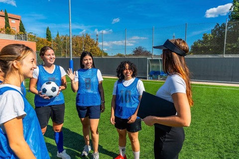 Women soccer players in blue pinnies listening attentively to their female coach explaining