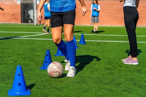 Young girl in a blue jersey practicing soccer dribbling skills around orange cones on a green
