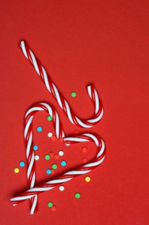 Candy canes and sugar confetti against red background, Christmas