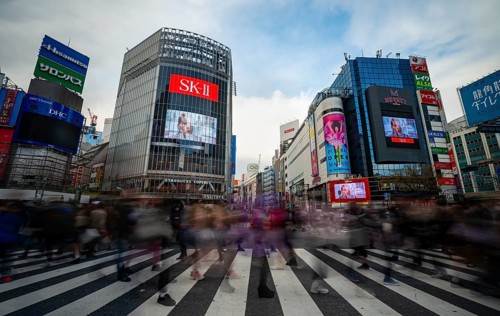 Crowd crossing zebra crossings on a large intersection, motion blur, modern houses with colorful
